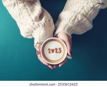 Happy New Year 2025 theme number 2025 over frothy surface of cappuccino served in white coffee mug holding by female hands on green background. Holidays food art, new year new you. (top view) - Powered by Shutterstock