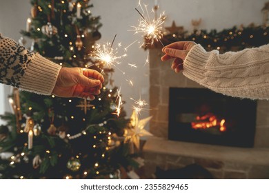 Happy New Year! Burning sparklers in hands on background of modern country fireplace and christmas tree with golden lights. Fireworks glowing in hands, couple celebrating in festive decorated room - Powered by Shutterstock