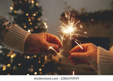 Happy New Year! Burning sparklers in hands on background of modern country fireplace and christmas tree with golden lights. Fireworks glowing in hands, couple celebrating in festive decorated room - Powered by Shutterstock