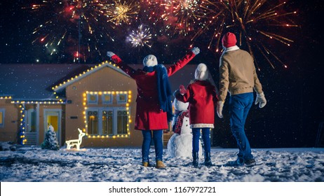 Happy New Year Celebration, Young Family Of Three Standing In The Front Yard Looking Into The Sky In The Eveningю House Decorated With Garlands For Christmas Eve.