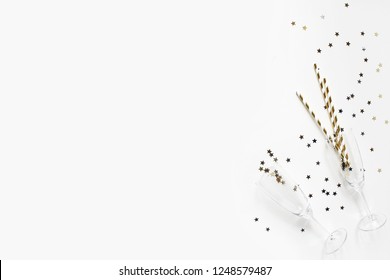 Happy New Year Composition. Champagne Glasses With Gold Confetti Stars And Drinking Straws On White Table Background. Party Concept. Flat Lay, Top View.