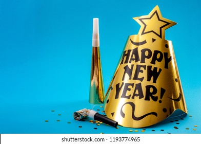 Happy New Year Concept With A Festive Hat, Noisemakers, Confetti, Party Blower  And Paper Trumpet Isolated On Blue Background With Copy Space