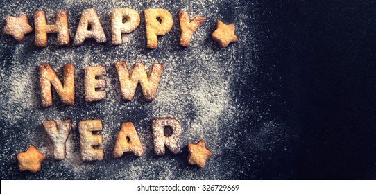 Happy New Year greeting with cookies letters on dark background with blank space 