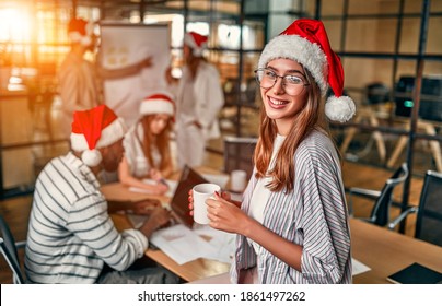 Happy New Year and Merry Christmas! Multiracial young creative people work in modern office wearing Santa hats. Handsome young woman with a cup of coffee on the last working day. - Powered by Shutterstock