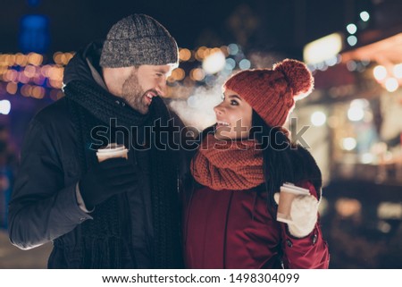 Happy new year! Photo of two cute people pair with hot beverage in hands celebrating x-mas evening raising mugs wearing warm jackets knitted hats and scarfs
