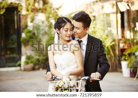 happy newly wed asian couple having fun riding a bicycle.