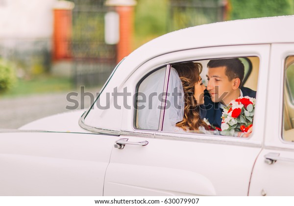 Happy newlywed couple kissing on a backseat of\
vintage car