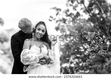 Happy newlyweds hug against the backdrop of a beautiful mountain landscape, the guy kisses the girl, the girl looks into the frame, black and white version