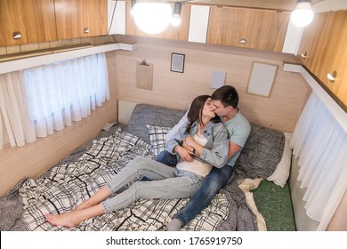 Happy Newlyweds Hug And Kiss Inside The Trailer Track On The Couch. A Honeymoon Trip Across The Country. Budget Vacation For A Young Family. Beautiful Couple Relaxing In The Camping. Concept Caravan