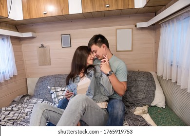 Happy Newlyweds Hug And Kiss Inside The Trailer Track On The Couch. A Honeymoon Trip Across The Country. Budget Vacation For A Young Family. Beautiful Couple Relaxing In The Camping. Concept Caravan