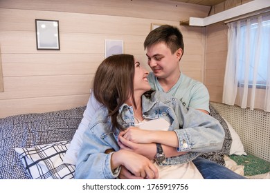 Happy Newlyweds Hug And Kiss Inside The Trailer Track On The Couch. A Honeymoon Trip Across The Country. Budget Vacation For A Young Family. Beautiful Couple Relaxing In The Camping. Concept Caravan