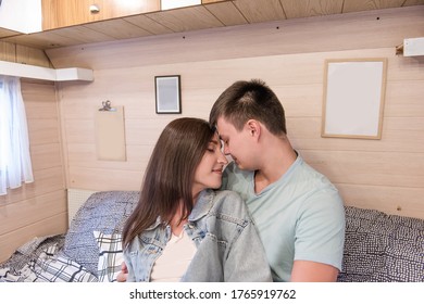 Happy Newlyweds Hug And Kiss Inside The Trailer Track On The Couch. A Honeymoon Trip Across The Country. Budget Vacation For A Young Family. Beautiful Couple Relaxing In The Camping. Concept Caravan