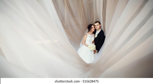 Happy newlyweds under the white curtains