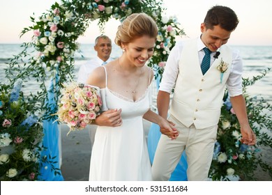 Happy newlyweds walk from wedding altar on the sea shore