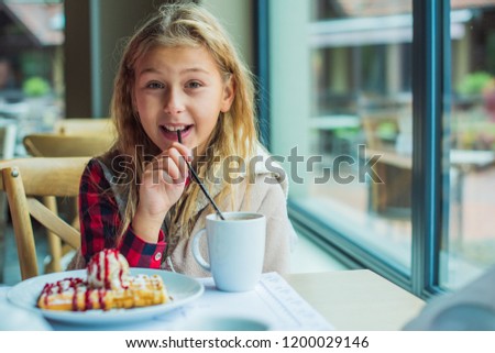 Happy nice little girl at cafe.The child sits at a table in a cafe and is happy.A happy childhood, concept of coziness and children, cold season, holidays
