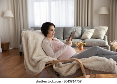 Happy Nine Months. Calm Young Pregnant Female Take Rest At Home Use Tablet Pc Check Electronic Lab Test Results Request Doctor Appointment Online. Relaxed Future Mother Engaged In Web Shopping On Pad