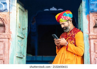 Happy North Indian Mature Man Wearing Colorful Outfits And Turban Using Smart Phone, Smiling Traditional Male Calling On Android Smart Mobile Phone.