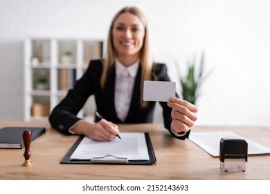 Happy Notary Holding Blank Business Card While Sitting On Blurred Background