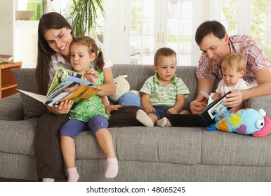 Happy Nuclear Family With Three Children Having Fun Sitting On Sofa At Home, Reading Books, Smiling.