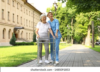 Happy nurse assisting elderly woman with walking frame at park - Powered by Shutterstock