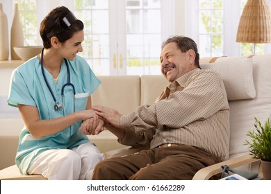 Happy Nurse Holding Hands Of Elderly Patient Sitting Side By Side At Home, Laughing.?