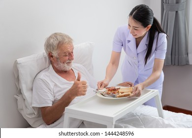 Happy nurse serving elderly senior man breakfast on bed in bedroom at nursing home, thumb up - Powered by Shutterstock