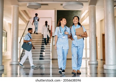 Happy nursing student and her Asian friend walking through a corridor at medical university.