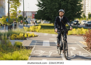 Happy office clerk in smart casual smiling, while riding after work in downtown. Front view of enjoyed entrepreneur cycling on bike lane, while returning home at sunny day. Concept of eco lifestyle. - Shutterstock ID 2266139343