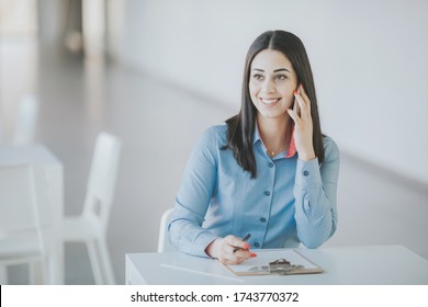 Happy Office Worker Making A Phone Call And Making Notes Ina Bright, White Office Space