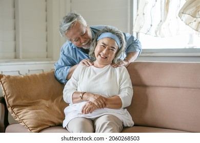 Happy Old Asian Husband Take Care And Massage Shoulder Elderly Wife Sitting On Sofa In Living Room At Home . Lovely Asia Senior Couple In Love Together On Couch 