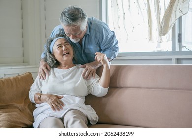 Happy Old Asian Husband Take Care And Massage Shoulder Elderly Wife Sitting On Sofa In Living Room At Home . Lovely Asia Senior Couple In Love Together On Couch 