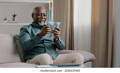 Happy old bald overweight African American senior mature elderly man happy with financial savings salary at home sitting couch. Winning online lottery holding dollars throw up cash money - Powered by Shutterstock