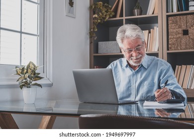 Happy old caucasian businessman smiling working online watching webinar podcast on laptop and learning education course conference calling make notes sit at work desk, elearning concept - Powered by Shutterstock