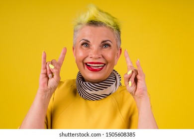 happy old cheerful female and a blue bandage on forehead,showing rocker gesture and grimace tongue and listen rock song on headphones.forever young soul.