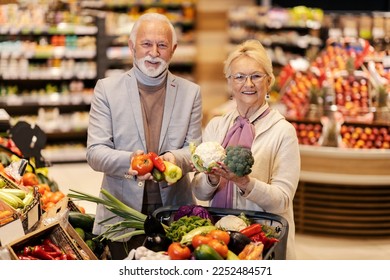 A happy old couple is buying fresh vegetables and holding it in hands while smiling at the camera. - Powered by Shutterstock