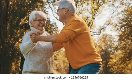 Happy Old Couple Dancing In Park. Senior Man Flirting With Elderly Woman. Romance At Old Age Autumn Day. High Quality Photo