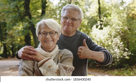 Happy Old Couple Hugging In Park. Senior Man Flirting With Elderly Woman. Thumbs Up. High Quality Photo