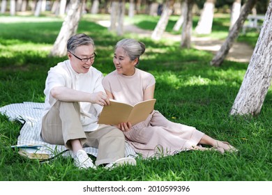 Happy Old Couple Sitting On The Park Grass Reading High Quality Photo