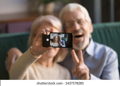 Happy old couple taking selfie on cellphone, smiling senior mature spouses middle aged wife and retired husband laughing holding phone make self portrait on smartphone camera, focus on mobile display - Powered by Shutterstock