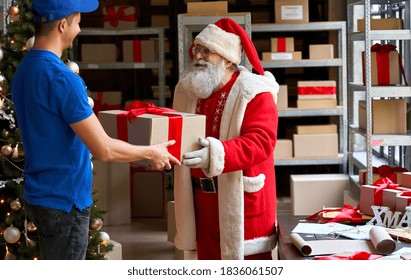 Happy Old Funny Bearded Santa Claus Wears Costume Holding Merry Christmas Present Giving Gift Box To Courier Worker Delivering Parcel Standing In Workshop. Xmas Fast Express Shipping Delivery Concept