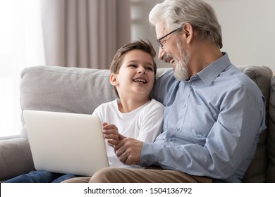 Happy old grandfather and little cute grandson laughing enjoying using laptop together sit on sofa, two age generations grandkid boy having fun with senior grandpa spend time with computer at home - Powered by Shutterstock