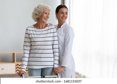 Happy Old Lady With Walker Stand Hug Female Nurse Or Caregiver Look In Distance Thinking Dreaming Of Healthy Future, Smiling Senior Mature Patient With Walking Frame And Woman Doctor Feel Hopeful