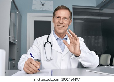 Happy Old Male Doctor Waving Hand Talking To Camera During Telehealth Consultation, Consulting Patient In Virtual Meeting, Telemedicine E Chat. Tele Medicine Videocall Visit, Headshot. Webcam View