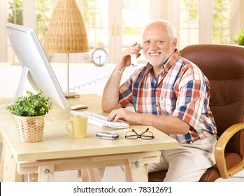 Happy Old Man On Landline Call Sitting At Desk Using, Computer, Smiling, Looking At Camera.?