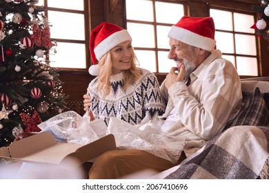 Happy old mature couple wearing santa hats unpacking Christmas shipping parcel opening box receiving shopping delivery package at home making holiday eve surprise presenting xmas gift at home. - Powered by Shutterstock