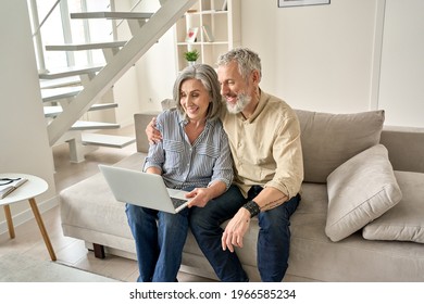 Happy old mid age family couple using laptop computer sitting on couch. Smiling senior mature husband and wife doing ecommerce online shopping, browsing web, watching tv, having video call at home. - Powered by Shutterstock