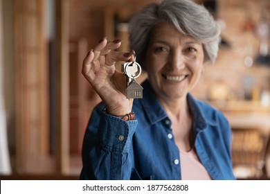 Happy old middle aged sincere beautiful hoary woman showing keys in hands, feeling excited of buying apartment or selling successfully dwelling, older people and real estate agency service concept.