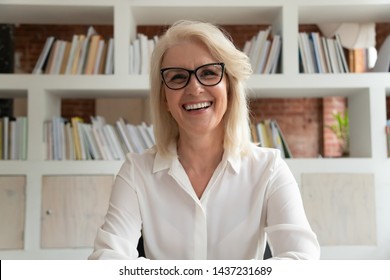 Happy old online teacher tutor look at camera give educational training class lecture teach by webcam, smiling mature business woman talk to webcam make video conference call sit at table in library - Shutterstock ID 1437231689