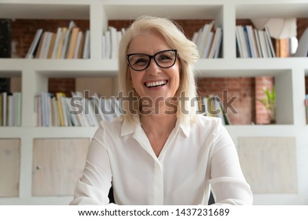Happy old online teacher tutor look at camera give educational training class lecture teach by webcam, smiling mature business woman talk to webcam make video conference call sit at table in library