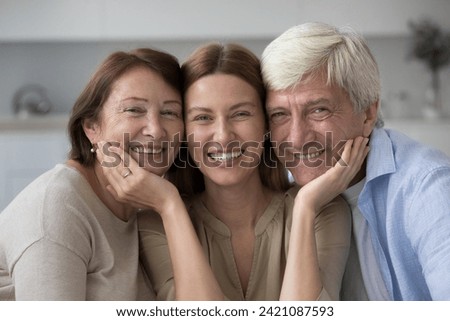 Happy old parents and cheerful beautiful adult daughter woman posing close with head touches, looking at camera with toothy smiles, laughing, enjoying family relationships, leisure time, closeness